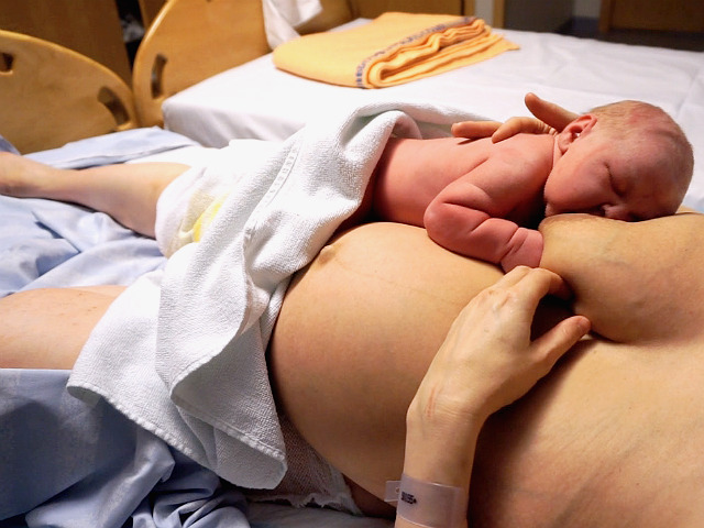 Stressen i förlossningsvården, amning. Nyfödd bebis ammar på mammans mage, BB.