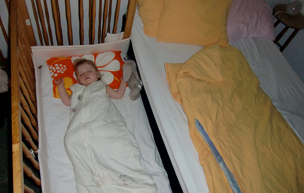 Säng för samsovning. Barn sover i spjälsäng med öppen sida, lik en bedside crib.