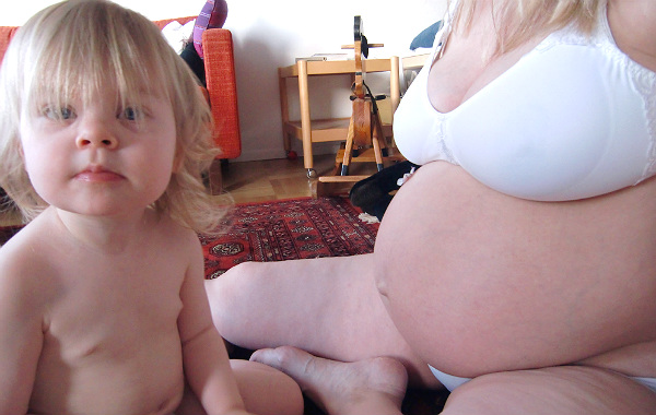 Nytt barn, ny amning. Liten flicka bredvid höggravid mamma. Båda sitter på golvet.