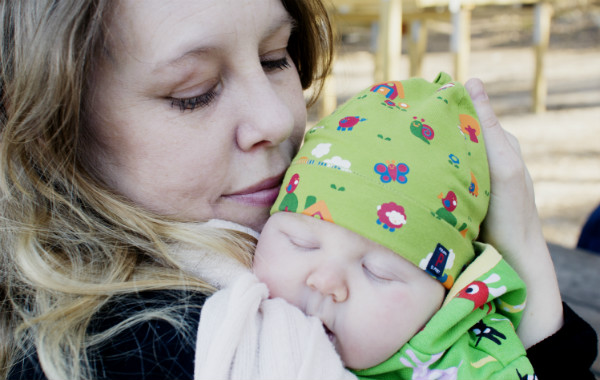 Tilläggsmata mindre, ge mindre ersättning. Liten bebis sover på mammans axel, utomhus.