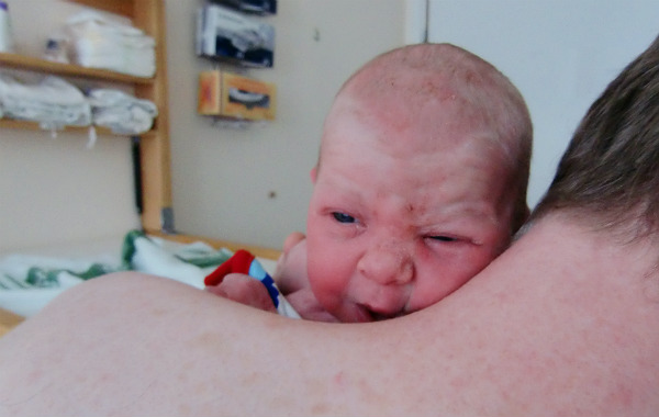 Tilläggsmata mindre, ge mindre ersättning. Nyfödd bebis med mun mot pappas axel, hungrig, ser ledsen ut.