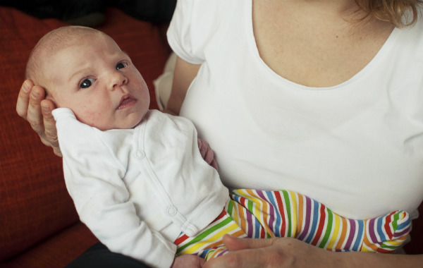 Tilläggsmata mindre, ge mindre ersättning. Mamma håller nyfödd bebis i famnen.