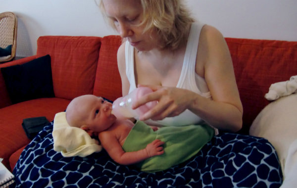 Tilläggsmata mindre, ge mindre ersättning. Mamma matar nyfödd bebis med flaska, i soffa.