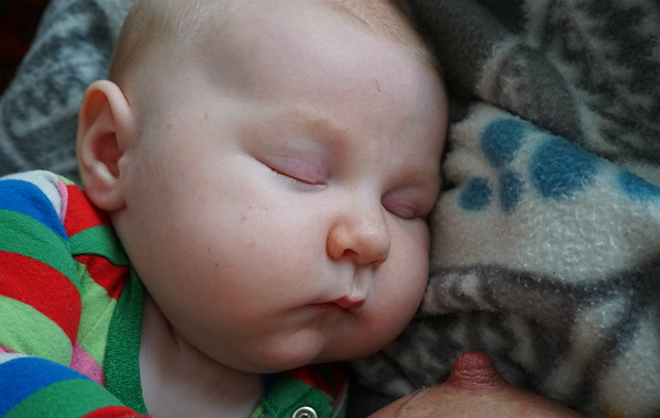 Mest förvirrande sakerna med amning. Liten bebis ligger på filt, sover. Bröstvårta skymtar.