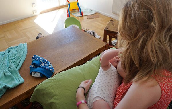 Mest förvirrande sakerna med amning. Bebis vid mammas bröst i soffa, stökigt vardagsrum.