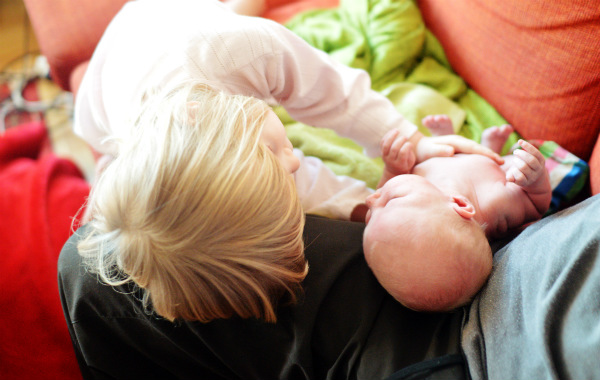 Mest förvirrande sakerna med amning. Större syskon klappar liten nyfödd bebis på soffa.