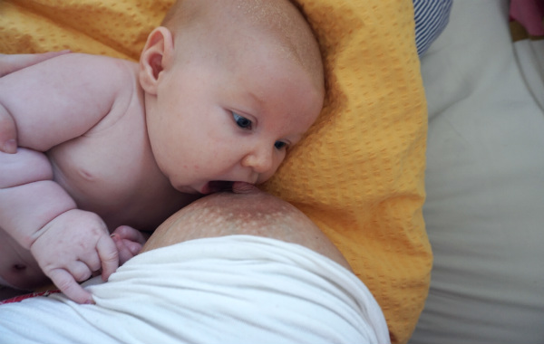 Mest förvirrande sakerna med amning. Bebis på säng, i färd med att börja amma. Gapar om bröstet.