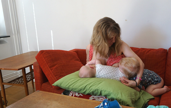 Tandemamning. Större syskon och bebis ammar samtidigt, på soffa.