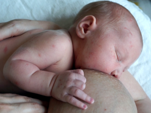 Amningsvänlig tilläggsmatning. Nyfödd ammar, håller en hand på bröstet och blundar.