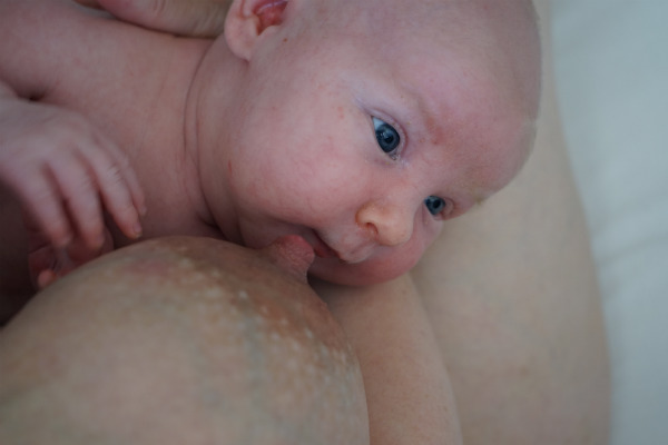 Amningsbildextra. Bebis och bröst i närbild, bebisen ler.