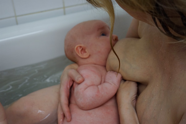 Amma i badkaret. Bebis ammar i badkaret i sin mammas famn.