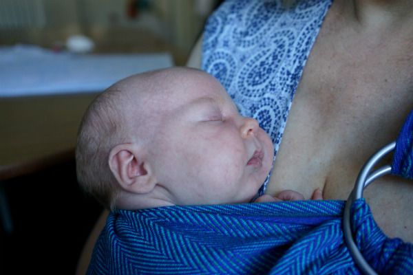 Sovande bebis i blå bärsjal på mammas bröstkorg.