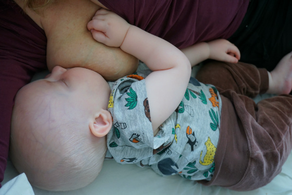 Matintroduktion. Bebis ammar liggande i säng med en hand på mammans bröst.