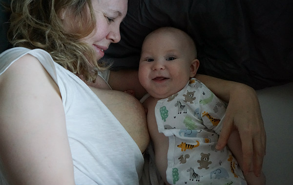 Matintroduktion. Bebis ligger i säng bredvid mamma, har just ammat. Ler mot kameran.