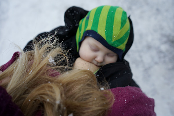 Matintroduktion. Bebis ammar utomhus, i snö, under mammans jacka.