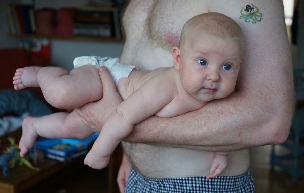 Man med bar överkropp bär en bebis, som ligger i famnen